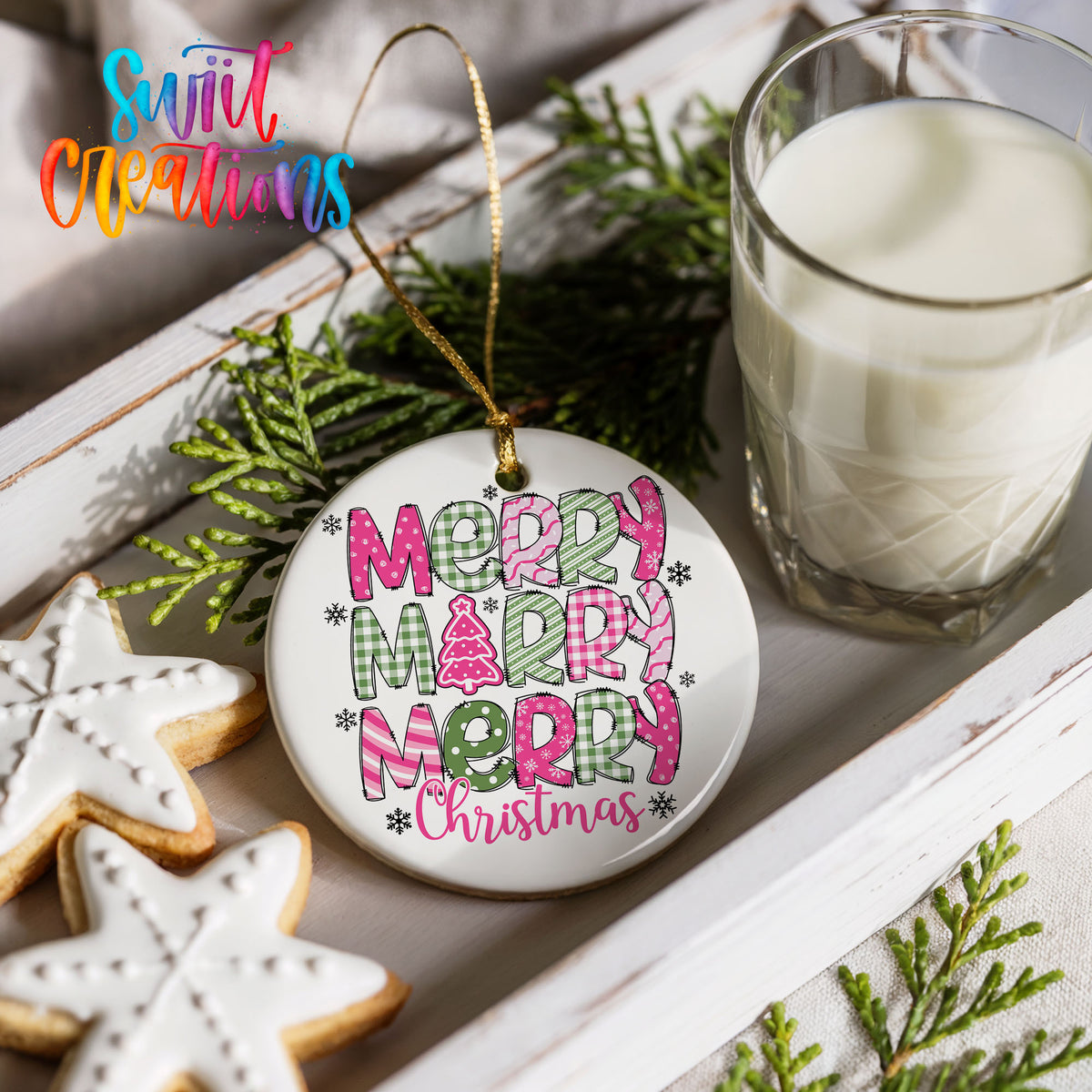 Round ceramic Christmas ornament featuring stacked patterned Merry Merry Merry Christmas lettering in pink and green, styled with cookies and milk