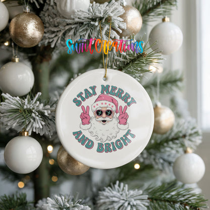 Round ceramic Christmas ornament featuring Santa in sunglasses giving peace signs with Stay Merry and Bright lettering, hanging on a frosted holiday tree
