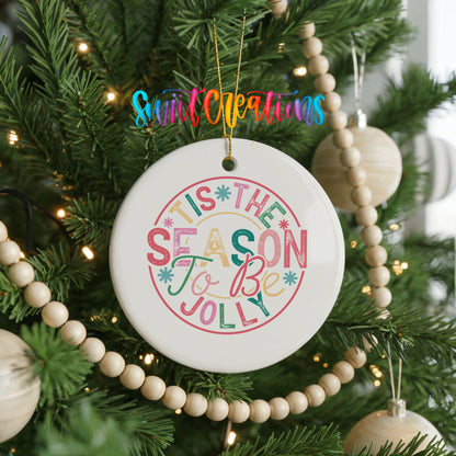 Round ceramic Christmas ornament featuring round pastel ’Tis the Season to Be Jolly holiday typography, hanging on a decorated Christmas tree