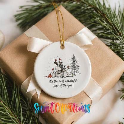 Round ceramic Christmas ornament featuring tipsy snowmen with wine glasses and It’s the Most Wonderful Wine of the Year lettering, placed on a wrapped Christmas gift
