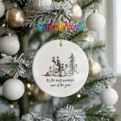 Round ceramic Christmas ornament featuring tipsy snowmen with wine glasses and It’s the Most Wonderful Wine of the Year lettering, hanging on a frosted holiday tree
