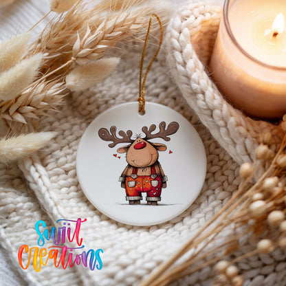 Reindeer in Red Plaid Overalls Christmas ornament styled beside a candle and cozy knit blanket