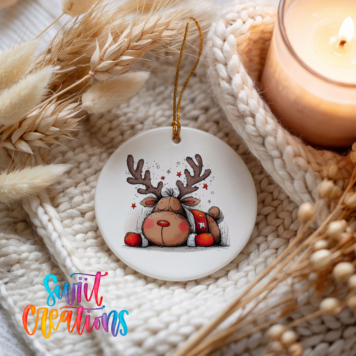 Cute Reindeer with Red Gift Bag Christmas ornament styled beside a candle and cozy knit blanket