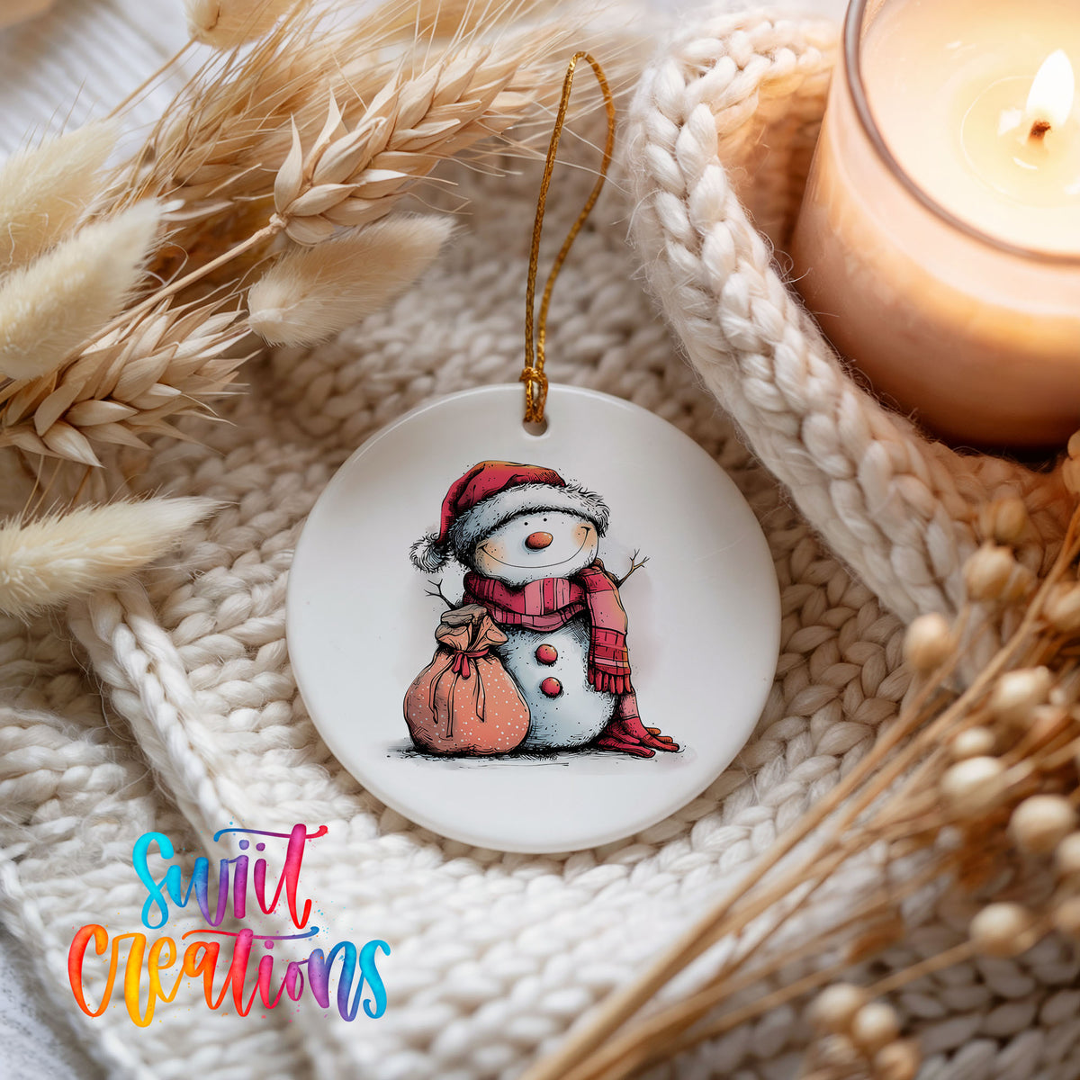 Snowman with Pink Gift Sack Christmas ornament styled beside a candle and cozy knit blanket