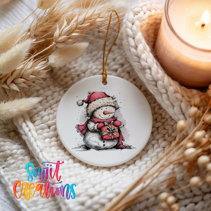 Snowman Holding a Christmas Heart Christmas ornament styled beside a candle and cozy knit blanket