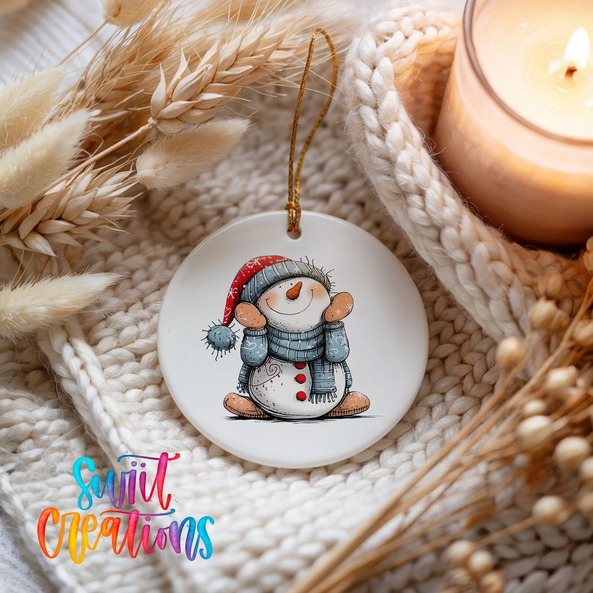 Snowman in Blue Hat and Scarf Christmas ornament styled beside a candle and cozy knit blanket