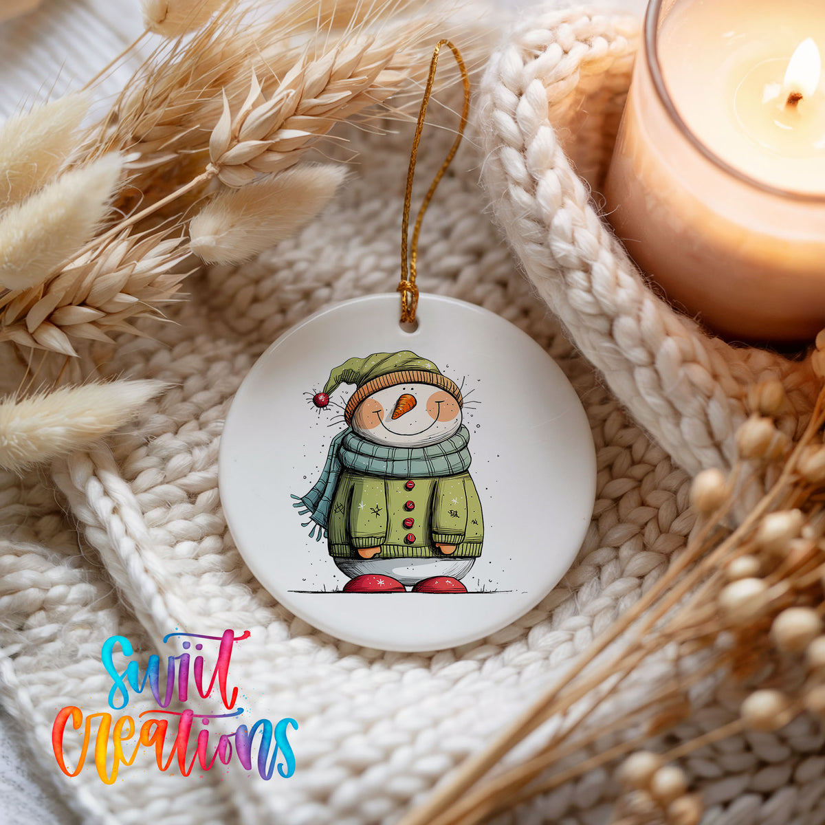 Snowman in Green Winter Coat Christmas ornament styled beside a candle and cozy knit blanket