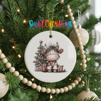 Highland cow beside a decorated Christmas tree and gifts ceramic Christmas ornament hanging on a green Christmas tree