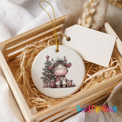 Highland cow beside a decorated Christmas tree and gifts ceramic Christmas ornament displayed in a wooden gift crate