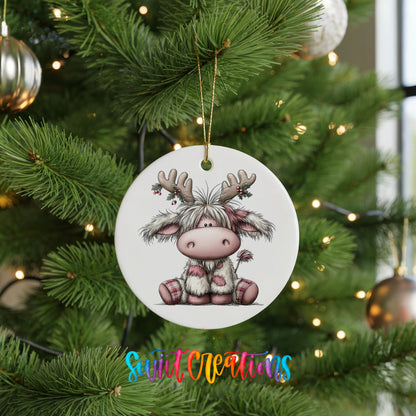 Highland cow wearing reindeer antlers and a striped scarf ceramic Christmas ornament hanging on a lit Christmas tree