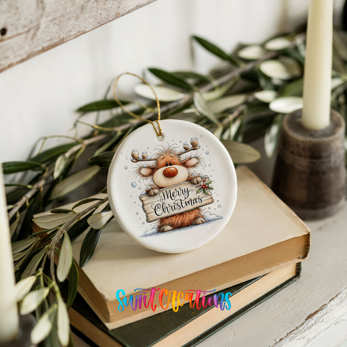 reindeer holding a Merry Christmas sign ceramic Christmas ornament styled on stacked books with greenery