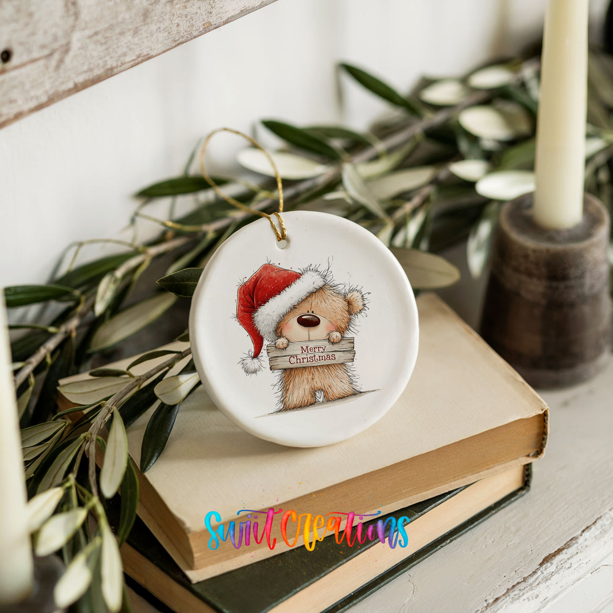 teddy bear in a Santa hat holding a Merry Christmas sign ceramic Christmas ornament styled on stacked books with greenery