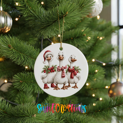 three Christmas geese wearing holiday wreaths ceramic Christmas ornament hanging on a lit Christmas tree