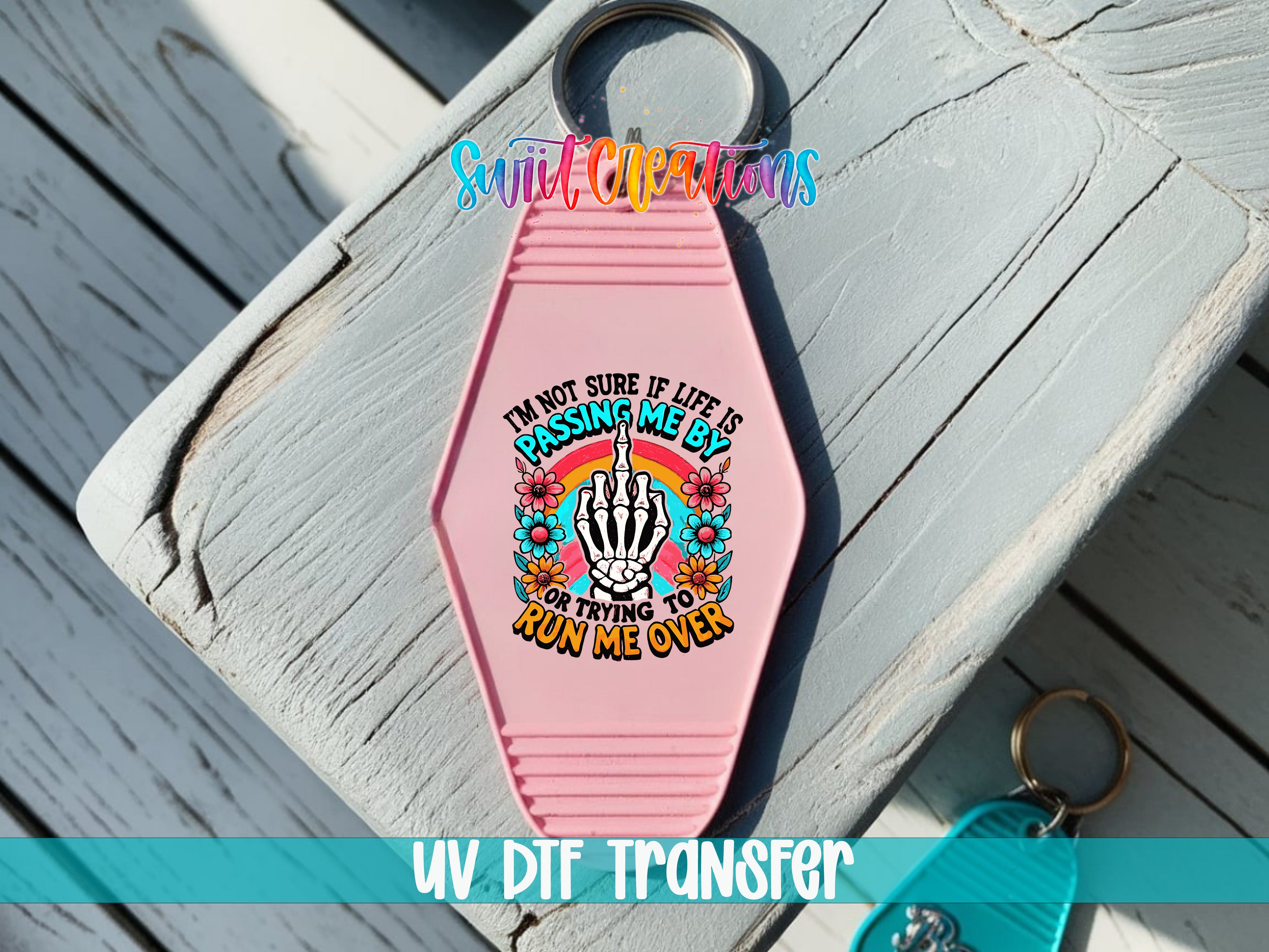 A pink keychain with a colorful graphic design and text, placed on a wooden surface.