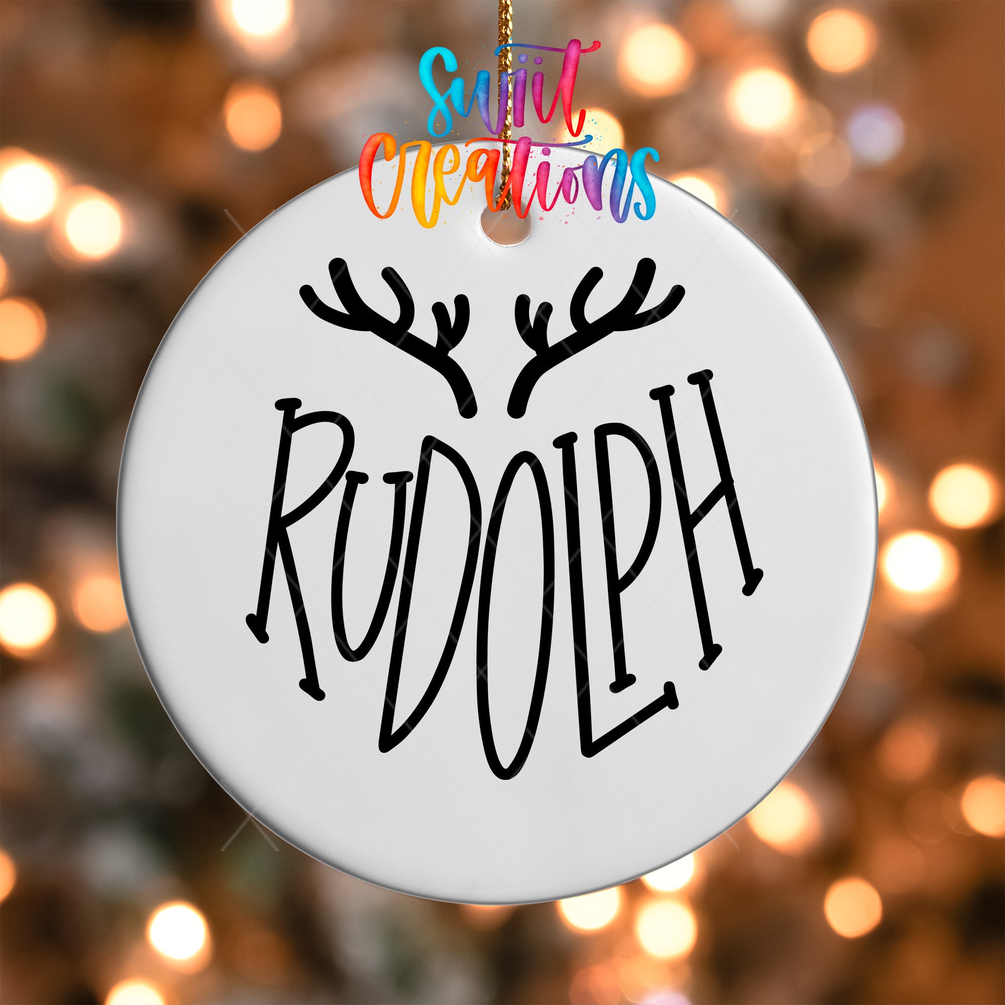 A white ornament with the word "RUDOLPH" written on it, hanging against a background of colorful lights.