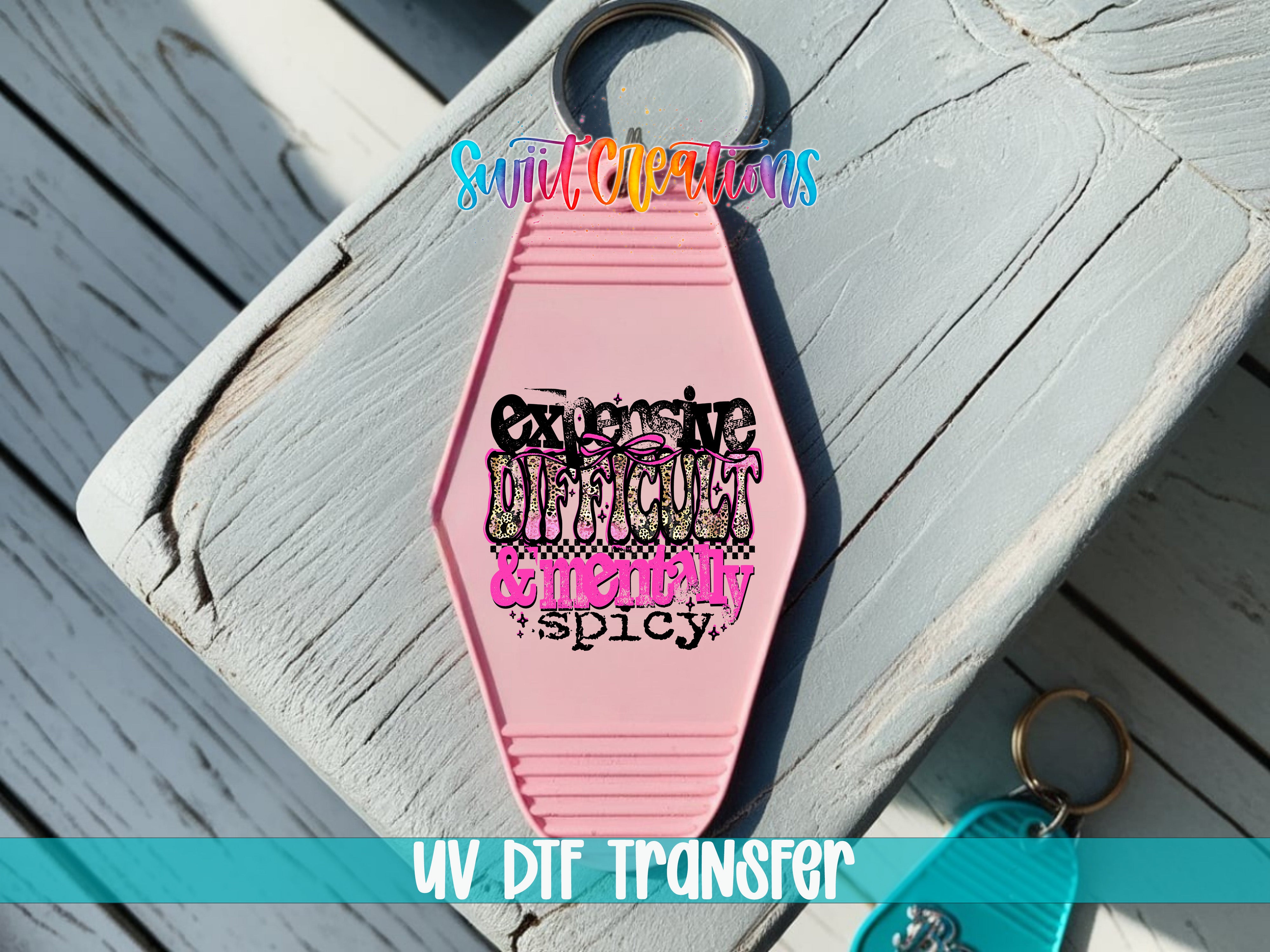 A pink keychain with a colorful design and text on it, placed on a wooden surface.