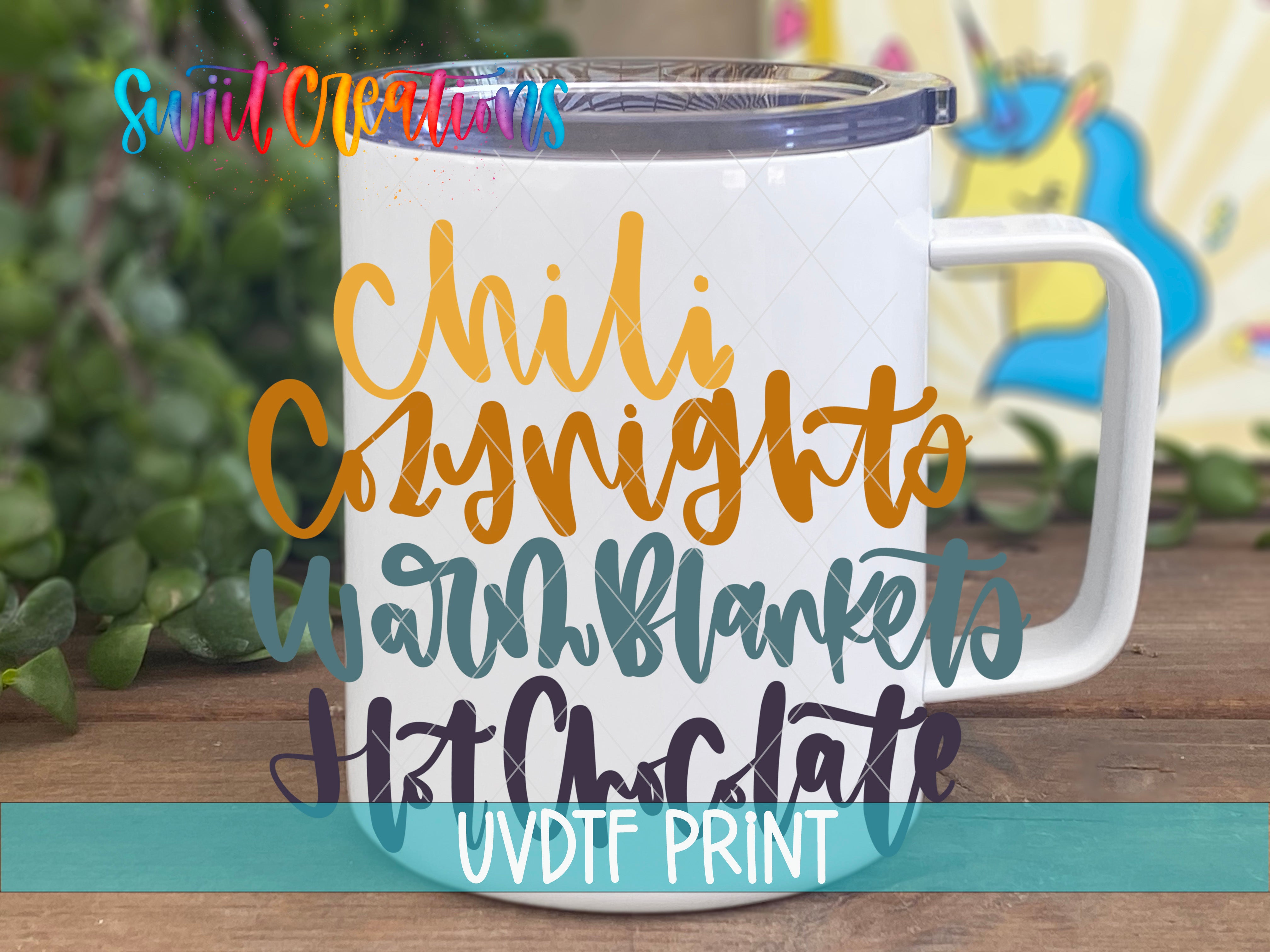 A white mug with colorful text printed on it, placed on a wooden surface with greenery in the background.