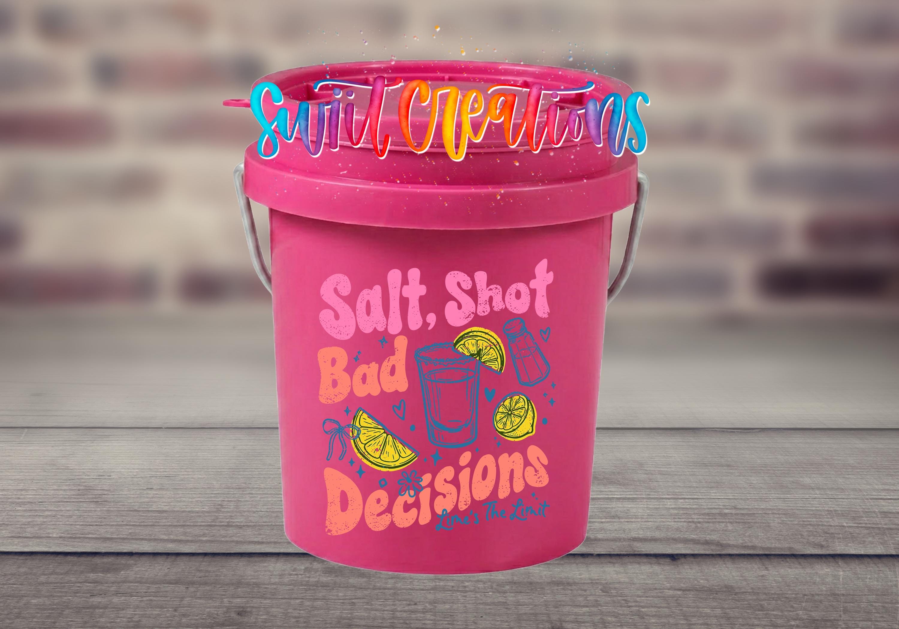 A pink bucket with a colorful design and text on it, placed on a wooden surface against a blurred brick wall background.