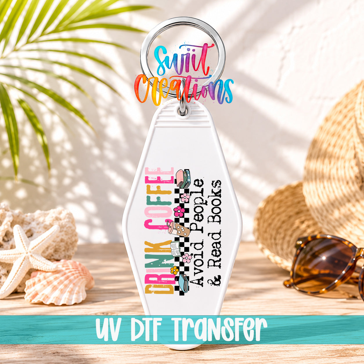 A keychain with a colorful design and text, placed on a wooden surface with sunglasses and a straw hat in the background.