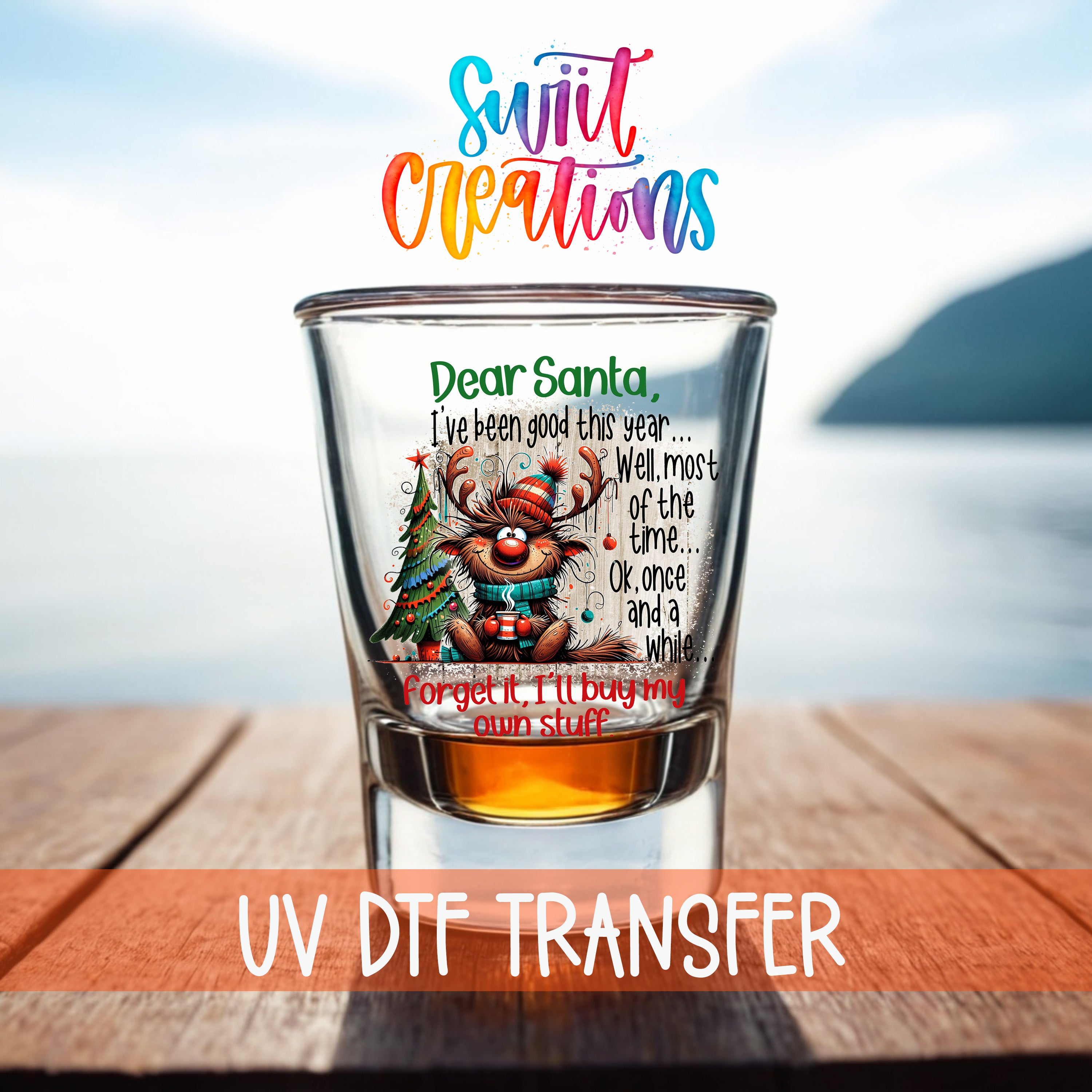 A glass with a colorful design featuring a reindeer and Christmas trees, along with a message that reads "Dear Santa, I've been good this year... Well, most of the time, OK, once and a while, Forget it, I'll buy my own stuff." The glass is placed on a wooden surface, with a body of water visible in the background.