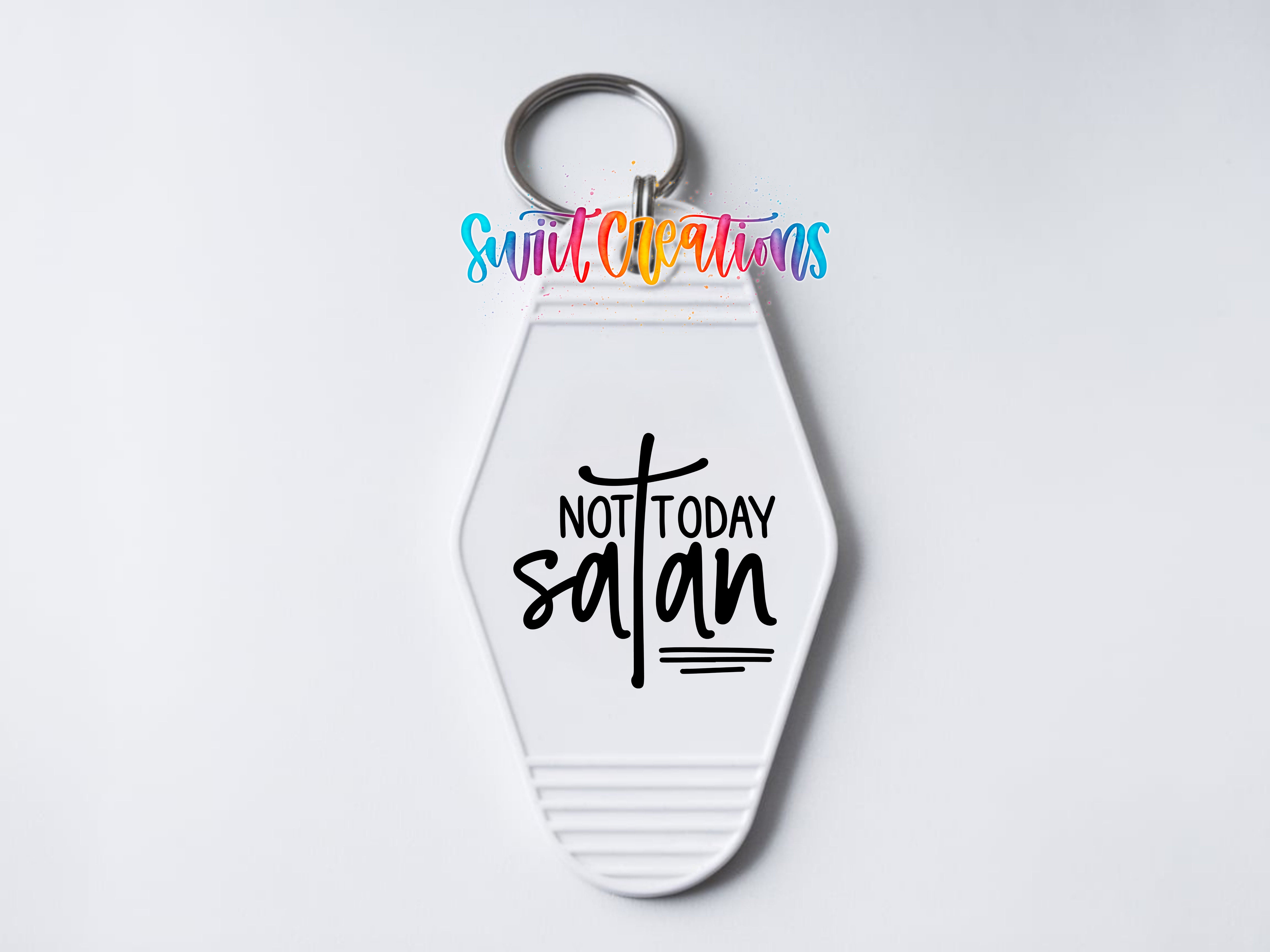 A keychain with a white hexagonal shape and a keyring attached to it. The keychain has a message printed on it that says "NOT TODAY SATAN".