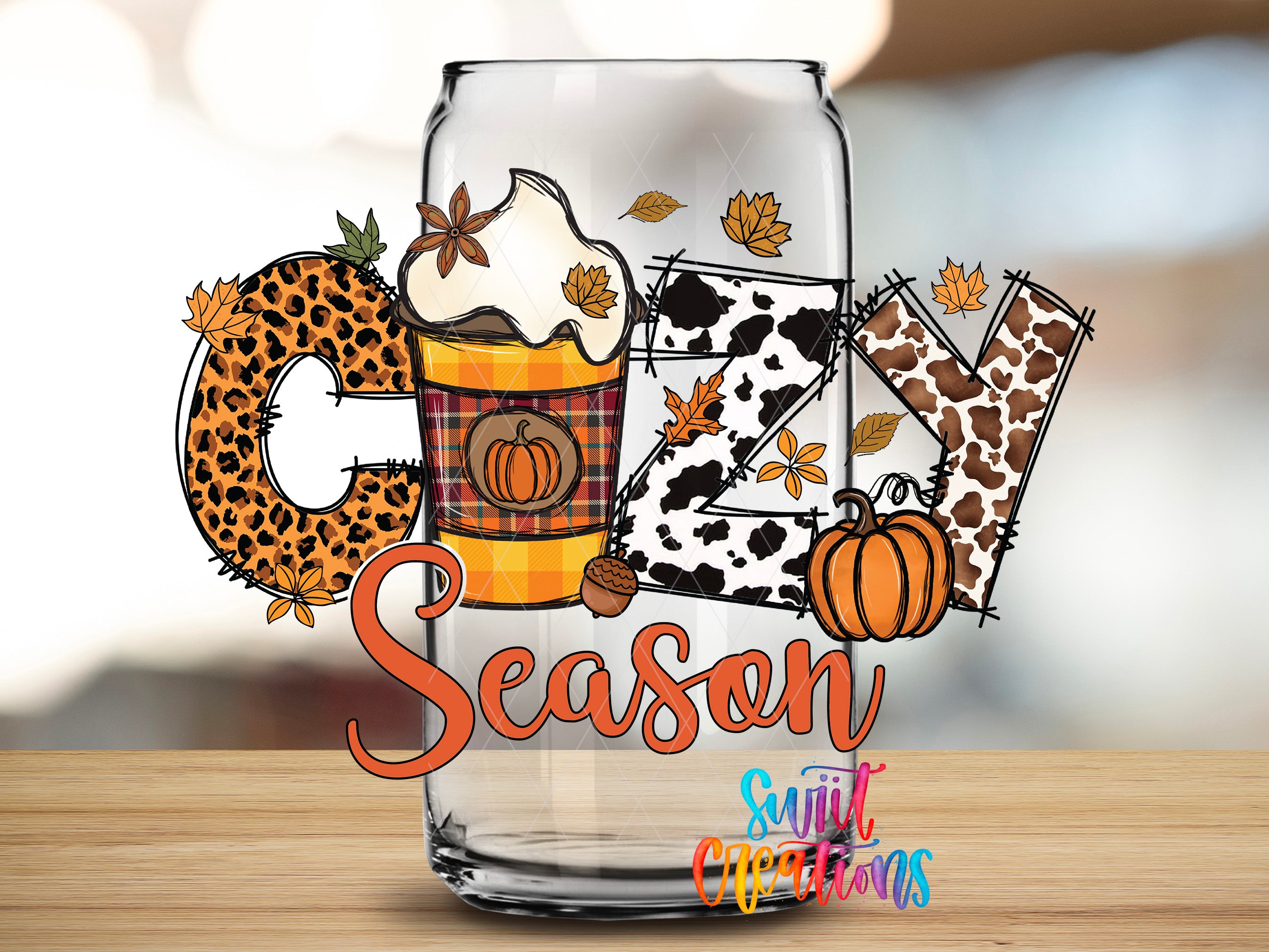 A glass can with the word "Cuddle" written on it, surrounded by various fall-themed elements such as a pumpkin, leaves, and a whipped cream cup.