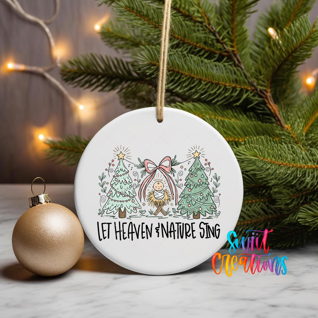 A white ceramic ornament with a Christmas tree design and the text "Let Heaven 'nature sing" is displayed on a marble surface, with a gold ornament and a string of lights in the background.