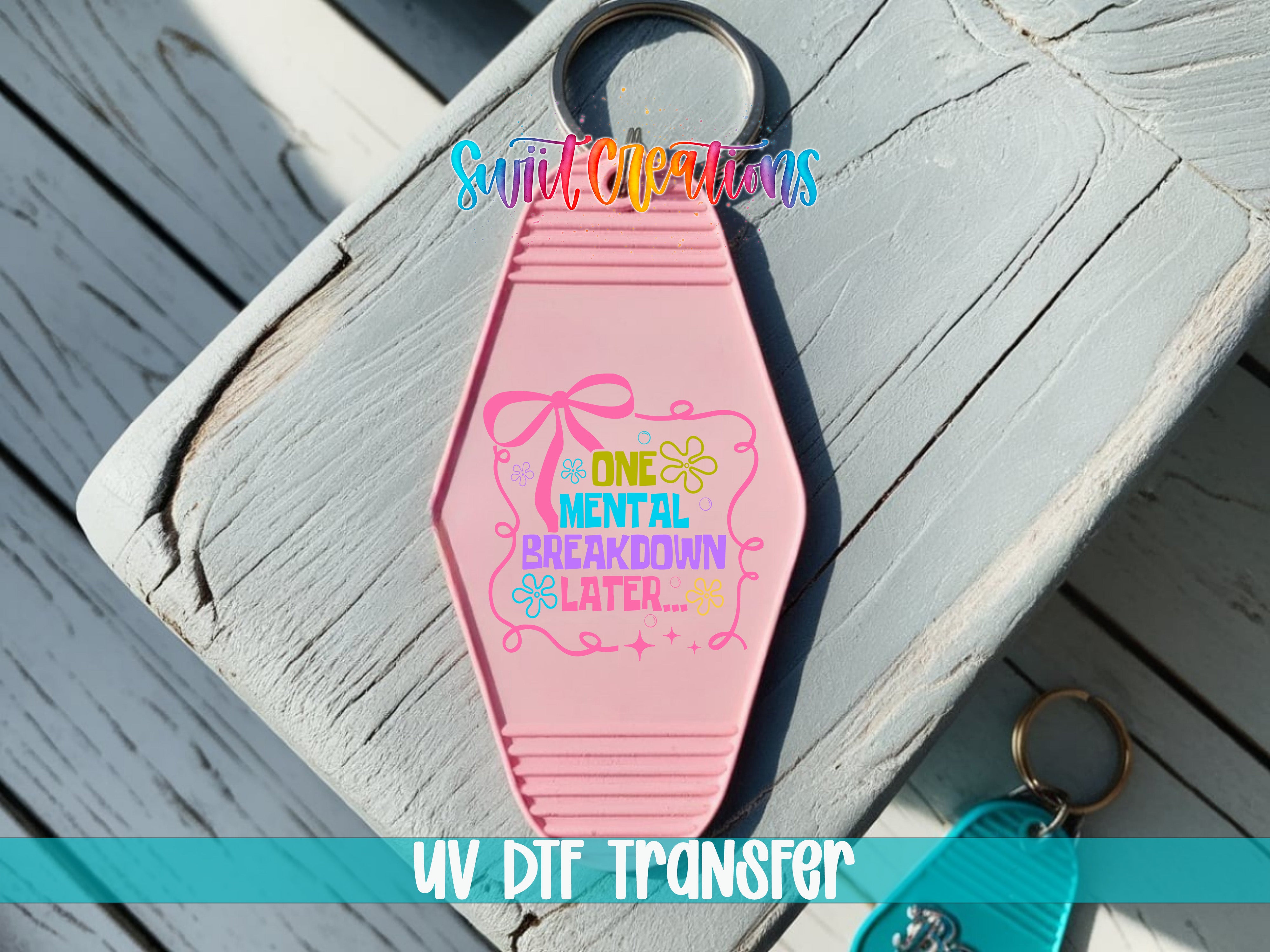 A pink keychain with a colorful design and text, placed on a wooden surface.