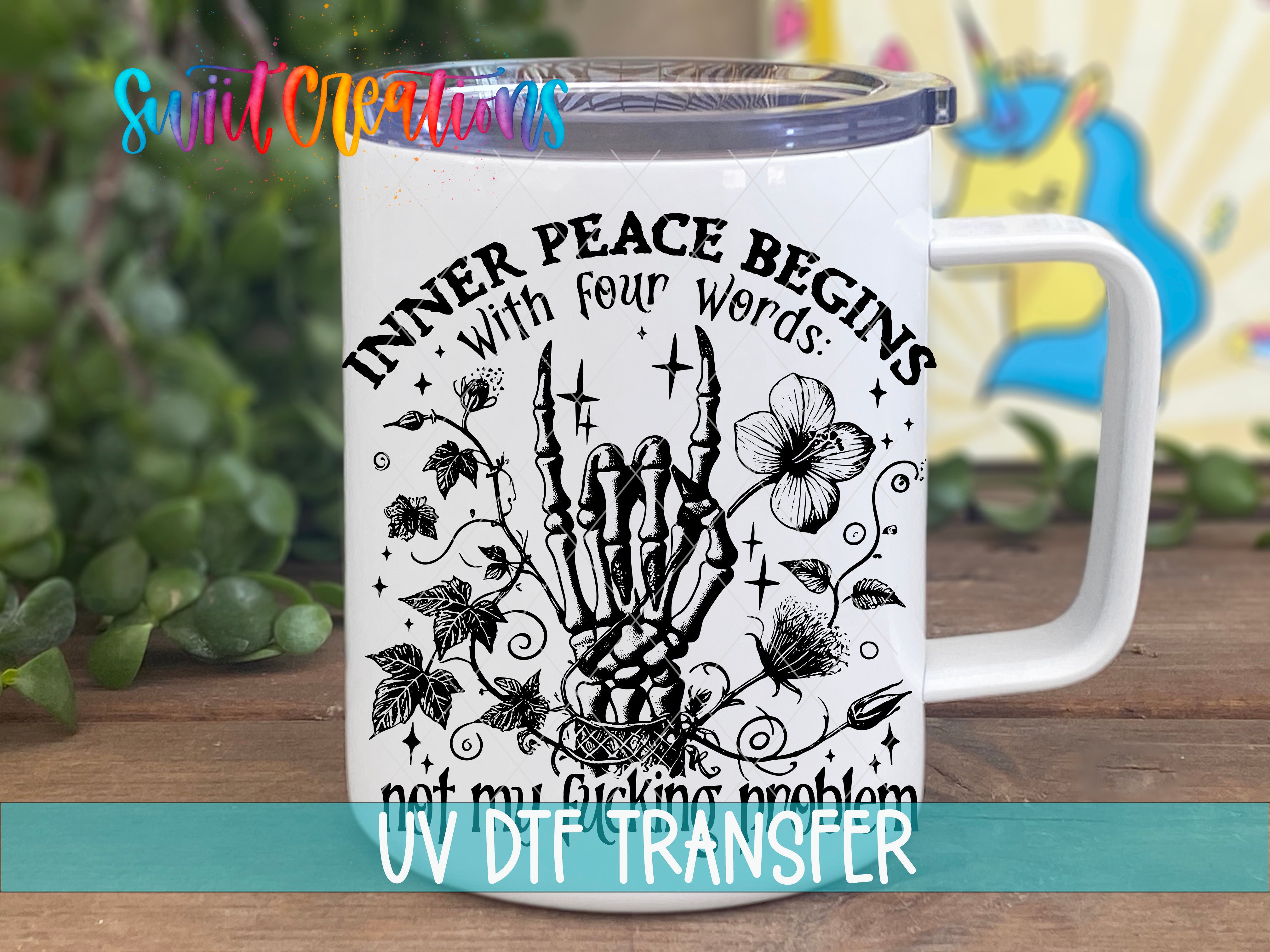 A white mug with a black and white illustration of a skeleton hand holding a flower, surrounded by leaves and vines, along with the text "INNER PEACE BEGINS WITH FOUR WORDS: not my fucking problem" printed on it.