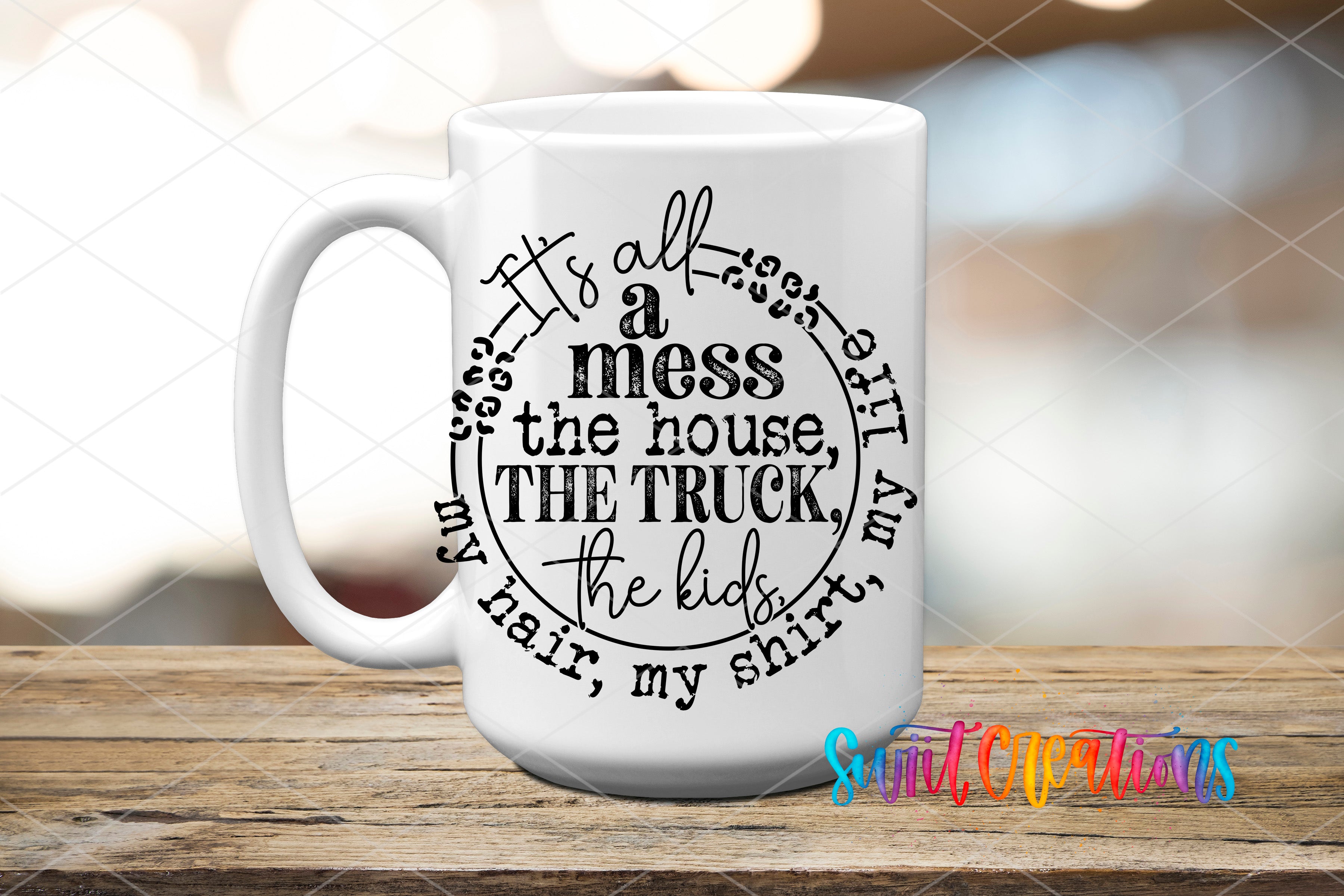 A white mug with a black text design that reads "It's all a mess the house, the truck, the kids, the hair, the shirt" arranged in a circular pattern.