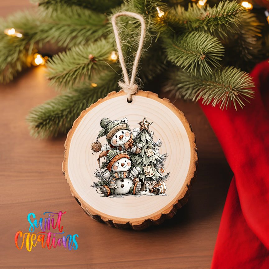 A wooden ornament featuring two snowmen is hanging on a Christmas tree, surrounded by pine branches and twinkling lights.