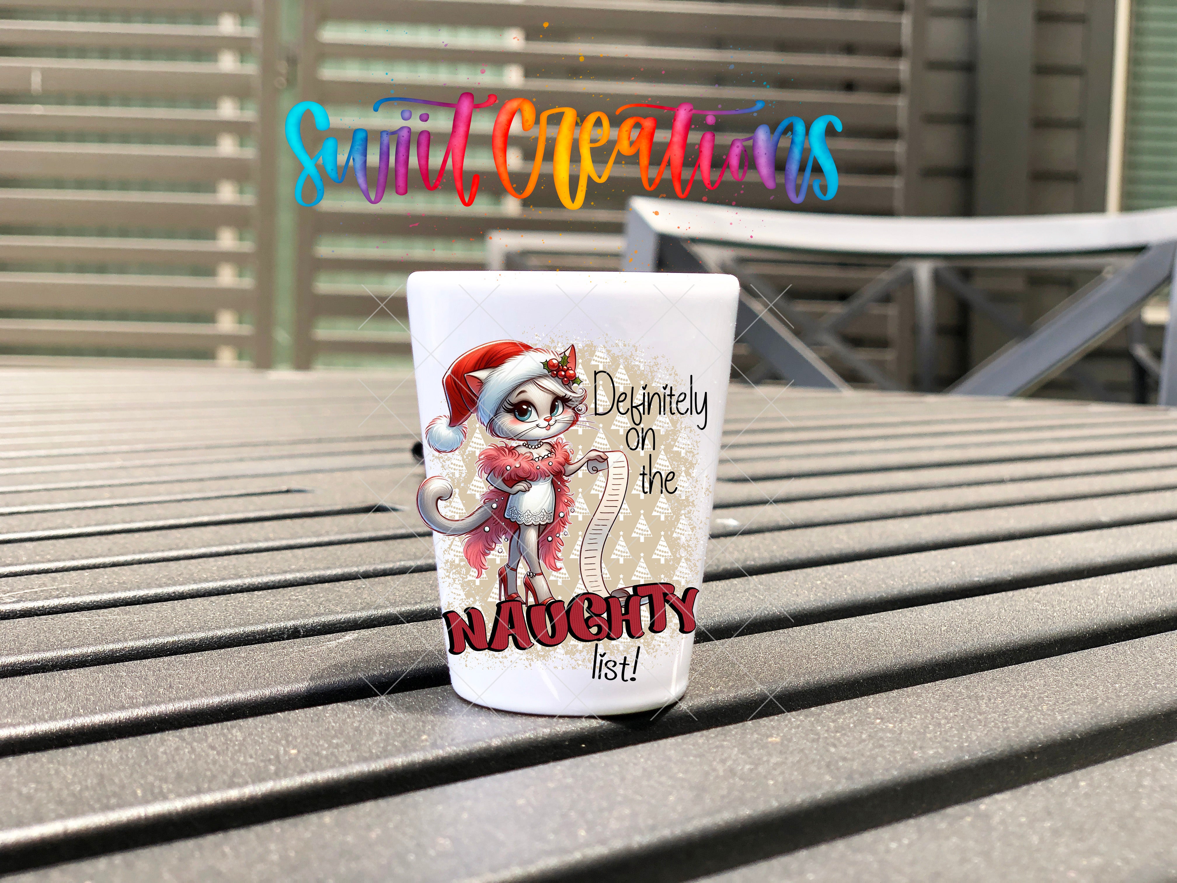A white mug with a cartoon cat and the text "Definitely on the Naughty list!" printed on it, placed on a wooden surface.