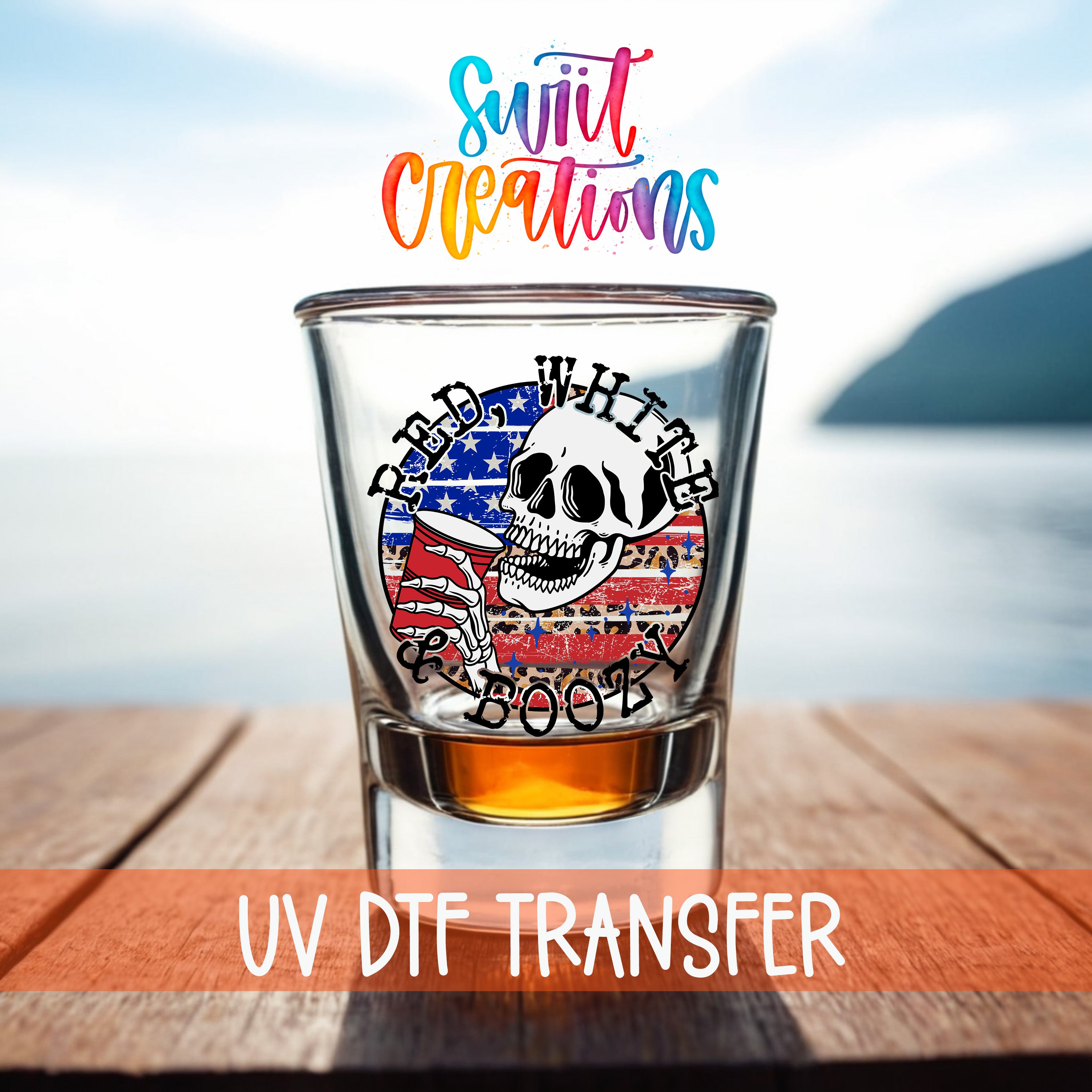 A shot glass with a skull design and an American flag pattern, placed on a wooden surface with a body of water in the background.