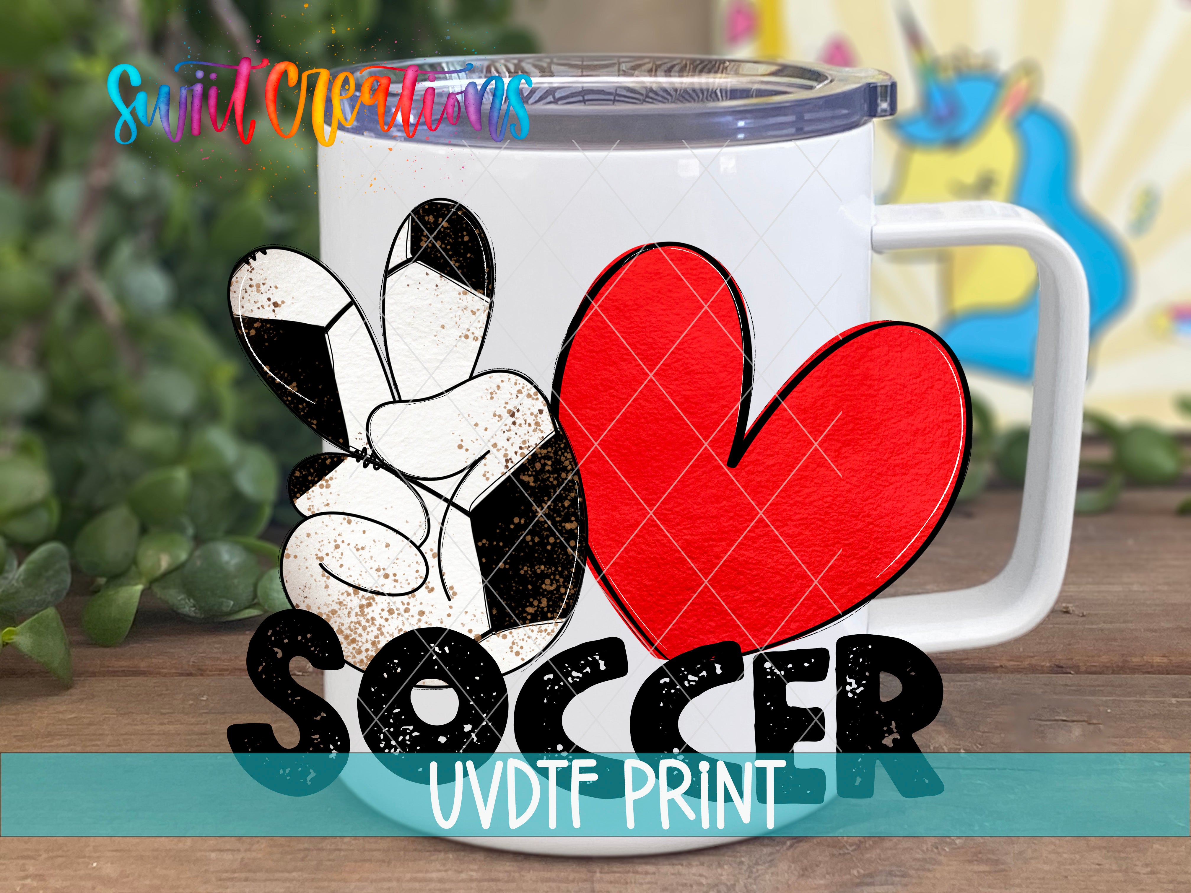 A white mug with a peace sign and a red heart, along with the word "SOCCER" printed on it, is displayed on a wooden surface.