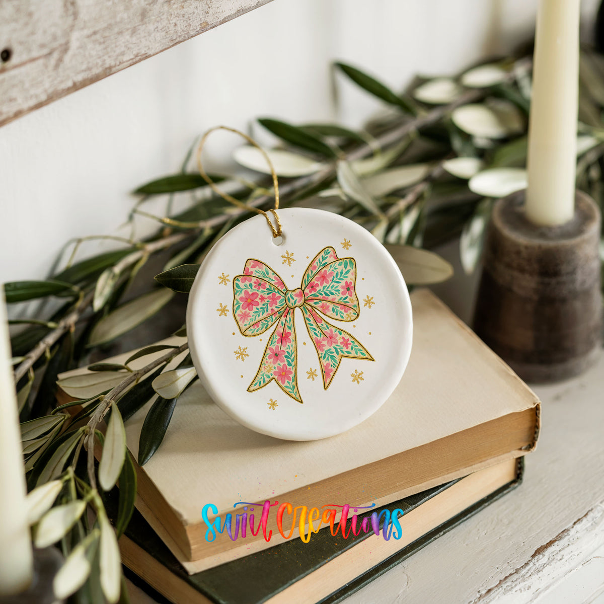 A white ceramic ornament with a floral design and a bow sits on top of two books, surrounded by greenery and a candle.