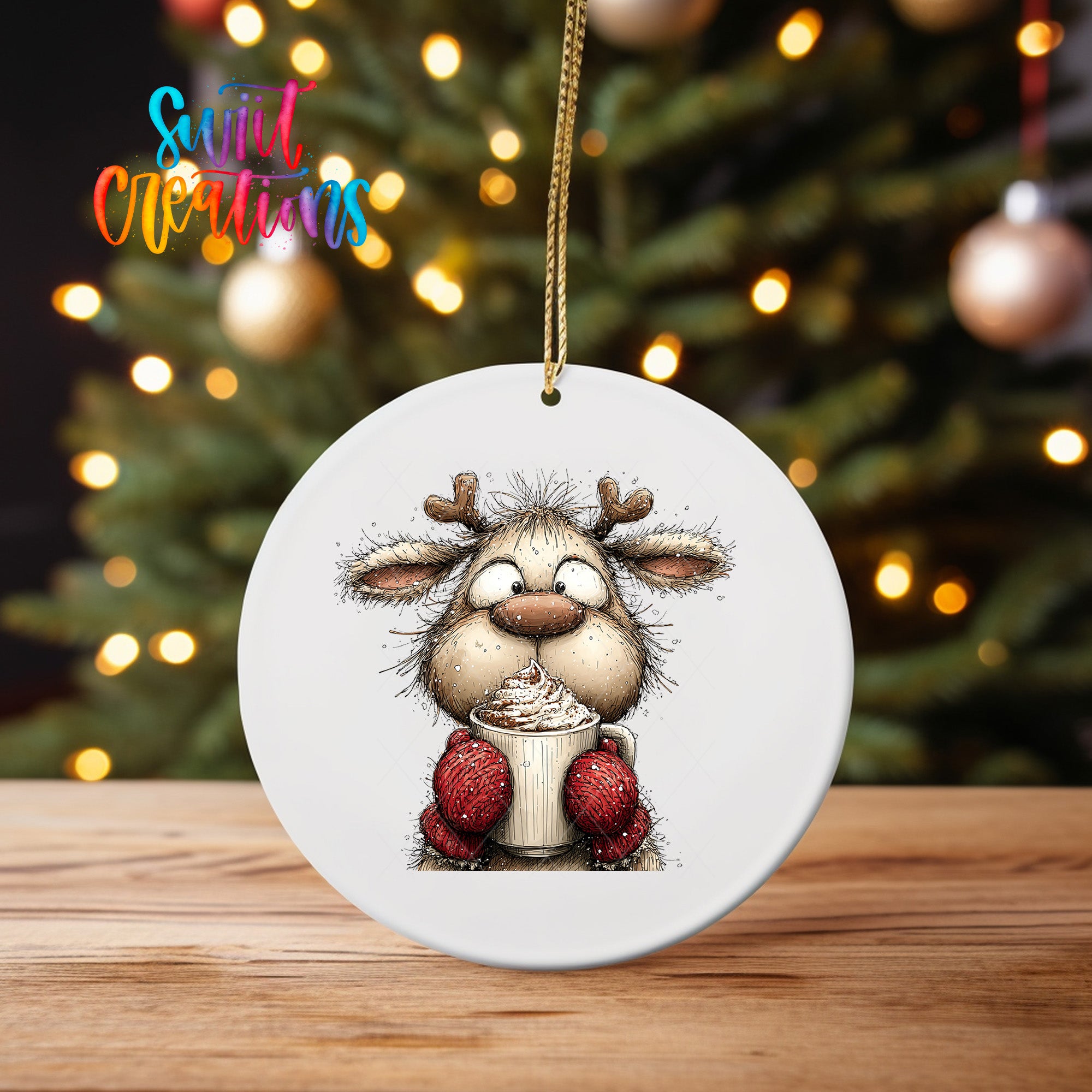 A white ceramic ornament featuring a cartoon reindeer holding a cup of hot chocolate, with a blurred background of a Christmas tree and colorful lights.