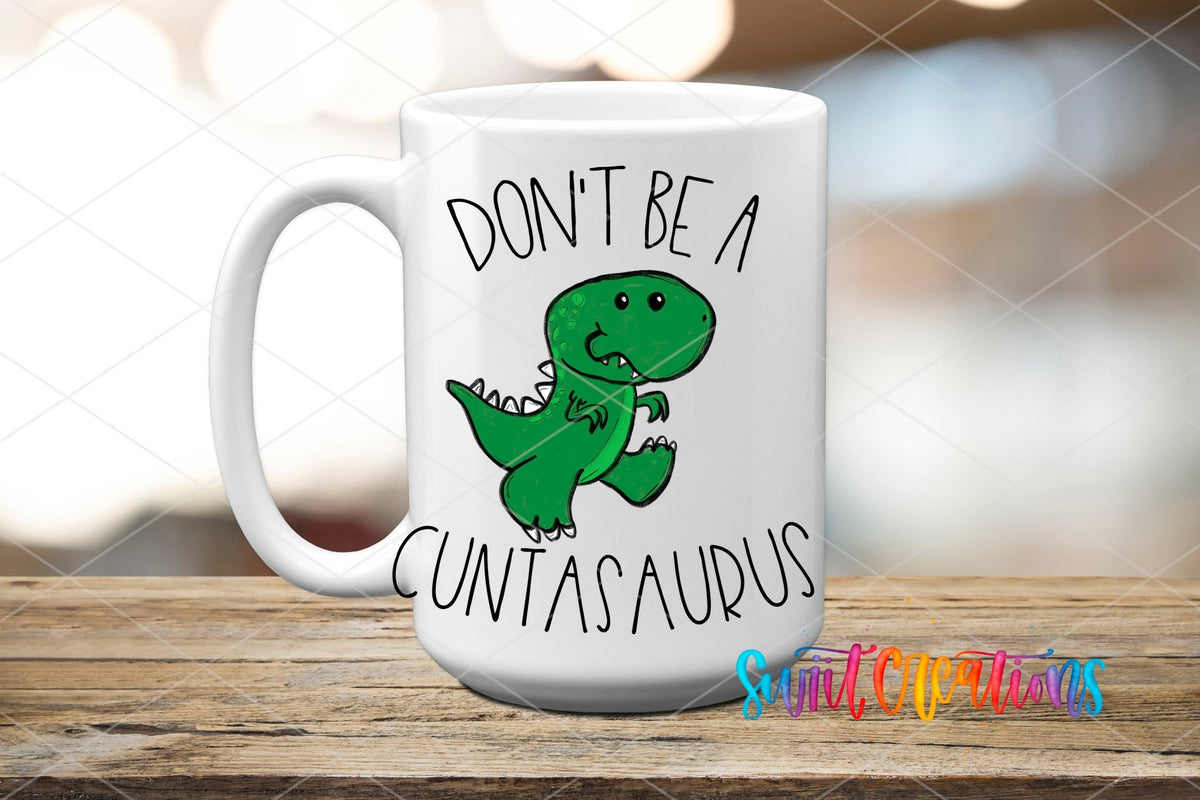 White mug displaying the Swiit Creations Don’t Be a Cuntasaurus UV DTF transfer with a funny green dinosaur.