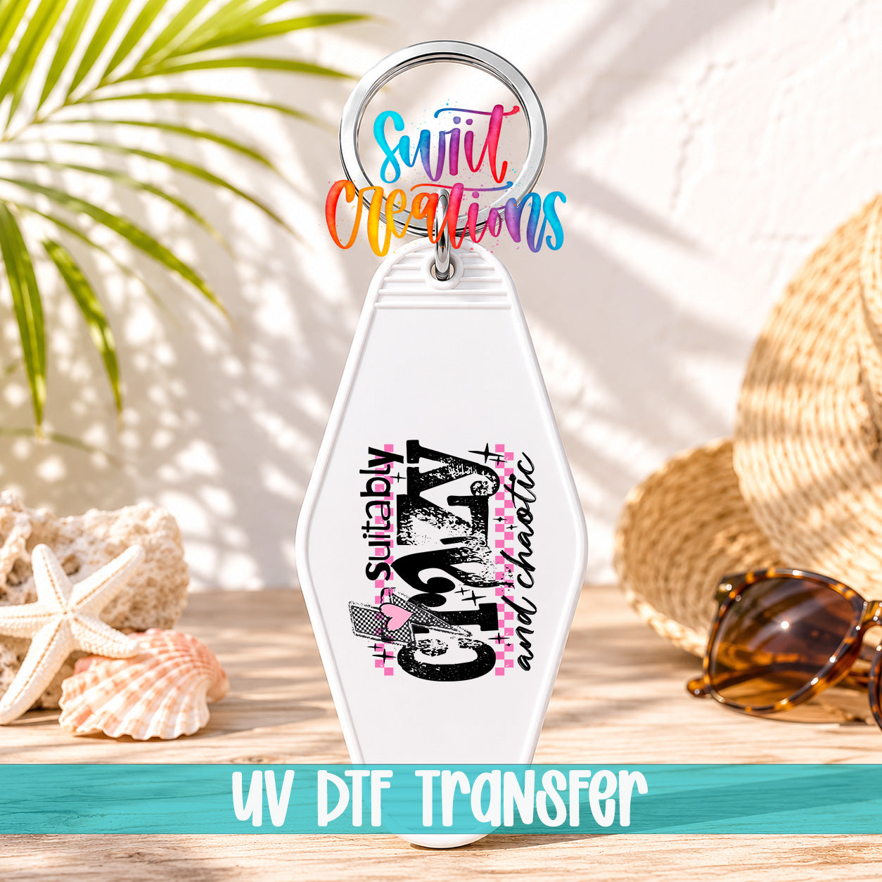 A keychain with a colorful design and text, placed on a wooden surface with sunglasses and a straw hat in the background.
