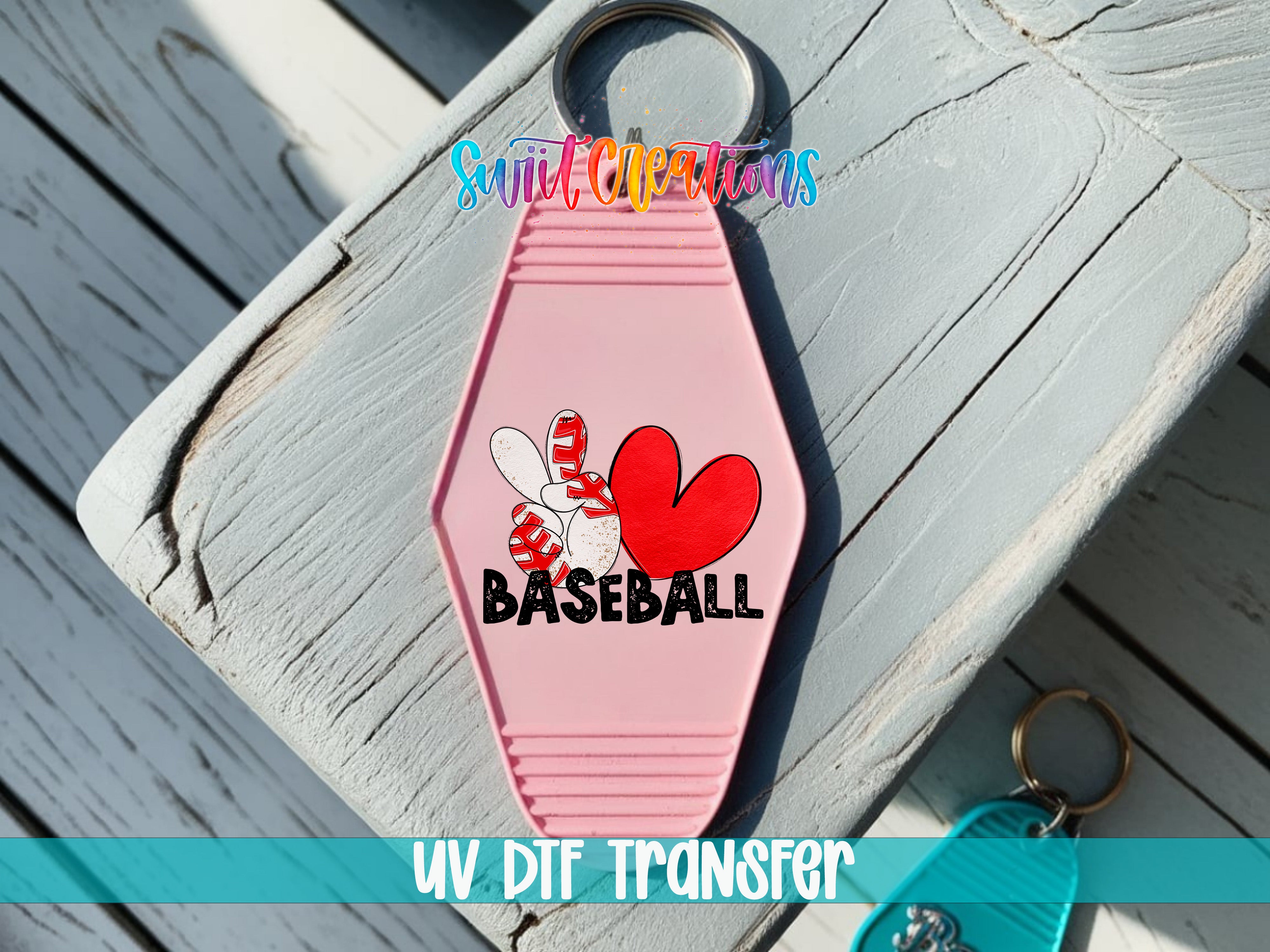 A pink keychain with a baseball design and the word "BASEBALL" printed on it, placed on a wooden surface.