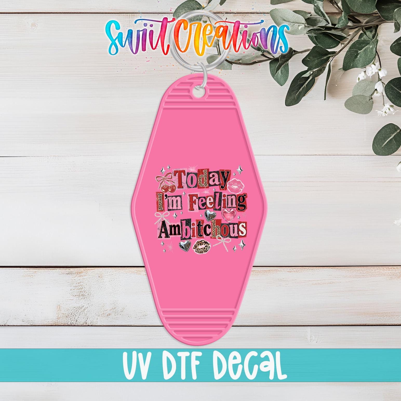 A pink keychain with the text "Today I'm feeling Amicky" printed on it, hanging on a wooden surface with some greenery in the background.