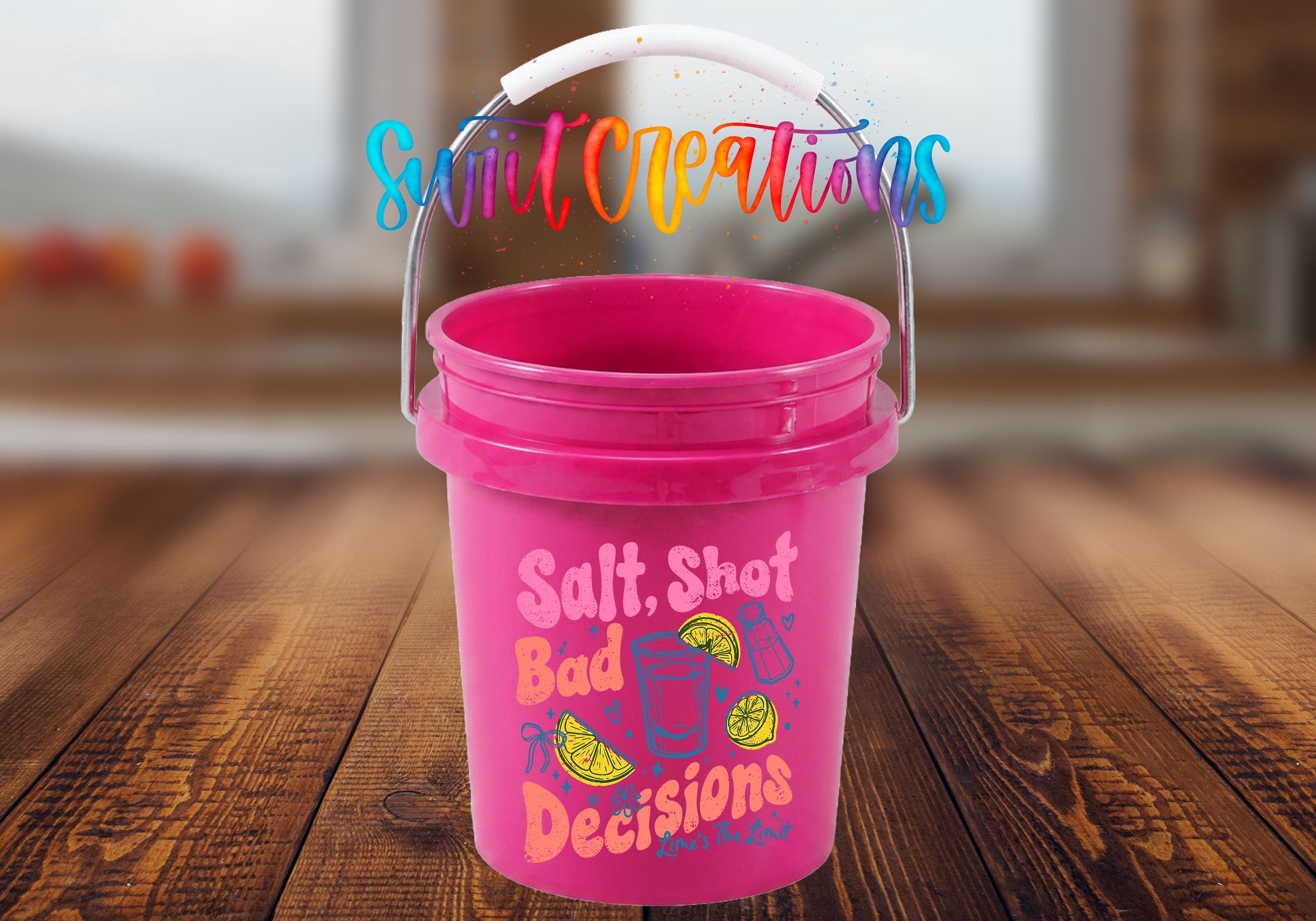 A pink bucket with a handle and a colorful, whimsical text design on it, placed on a wooden surface.