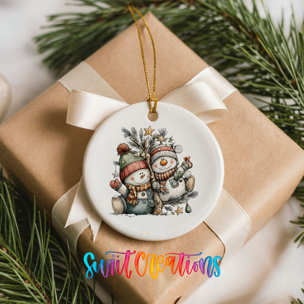 A white ceramic ornament with a snowman and pine tree design, hanging from a ribbon on a gift box.