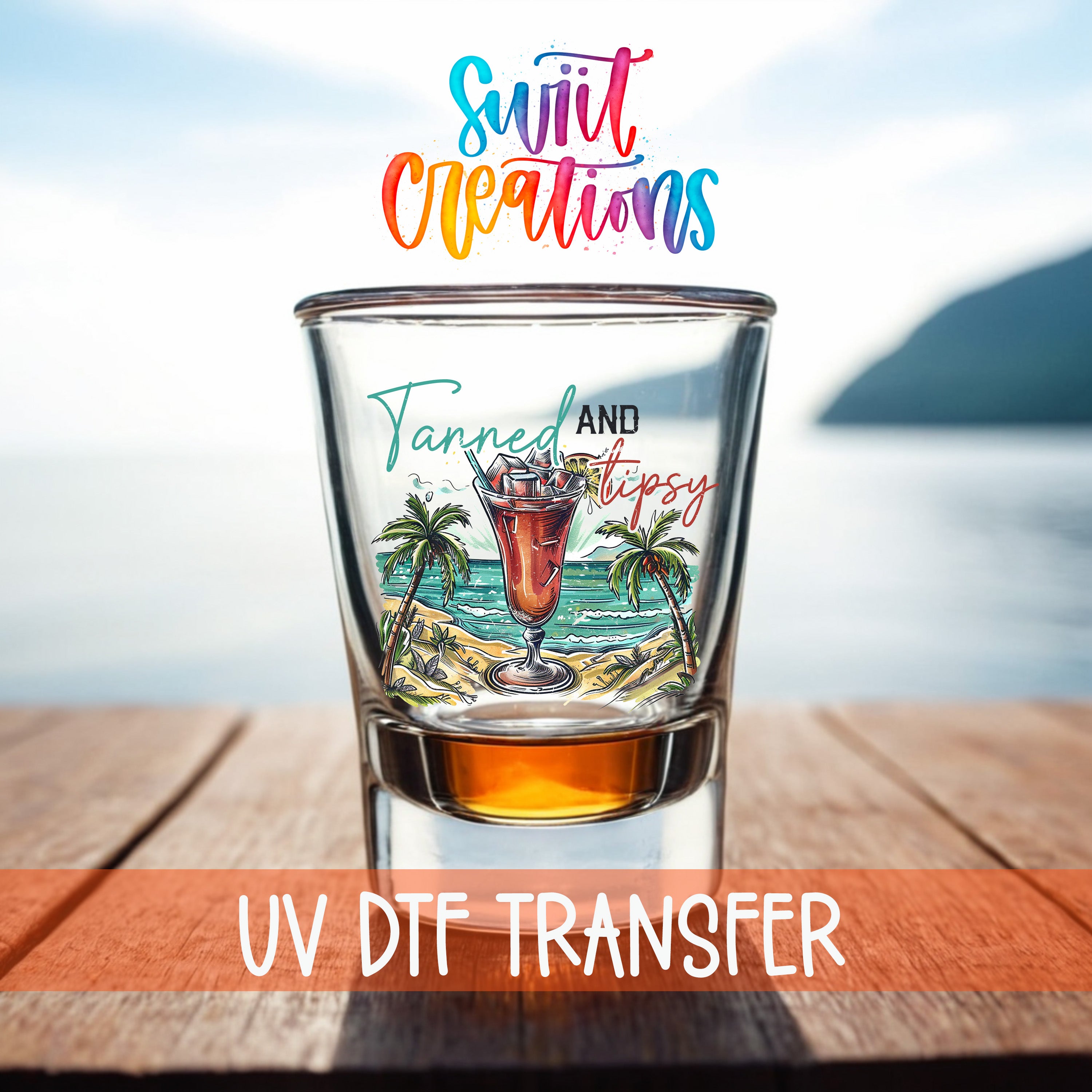 A shot glass with a tropical beach scene and a cocktail illustration, placed on a wooden surface with a body of water in the background.