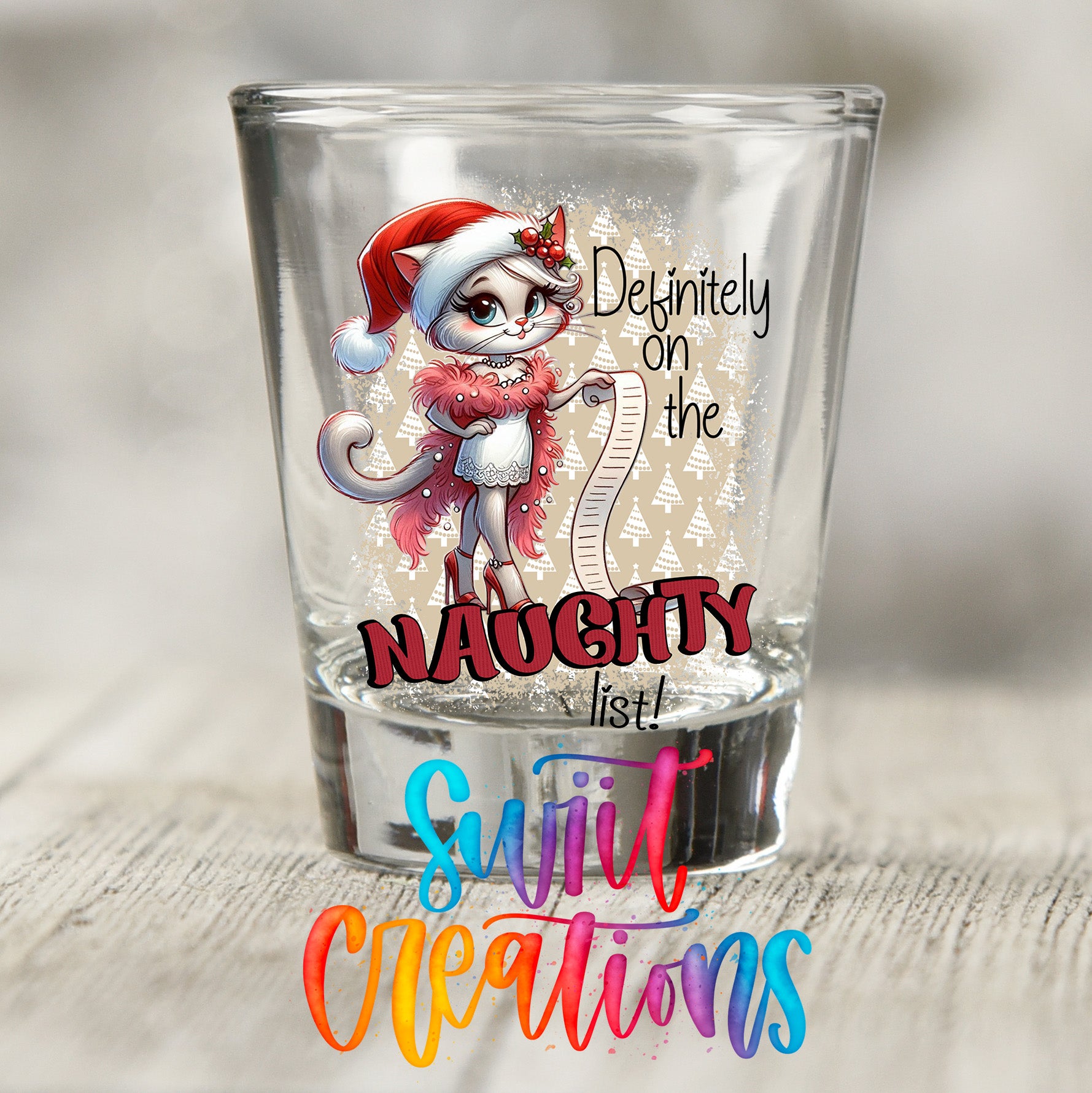 A glass shot glass with a cartoon image of a cat wearing a Santa hat and holding a list, along with the text "Definitely on the Naughty list!" and "Suit Creations" written below.
