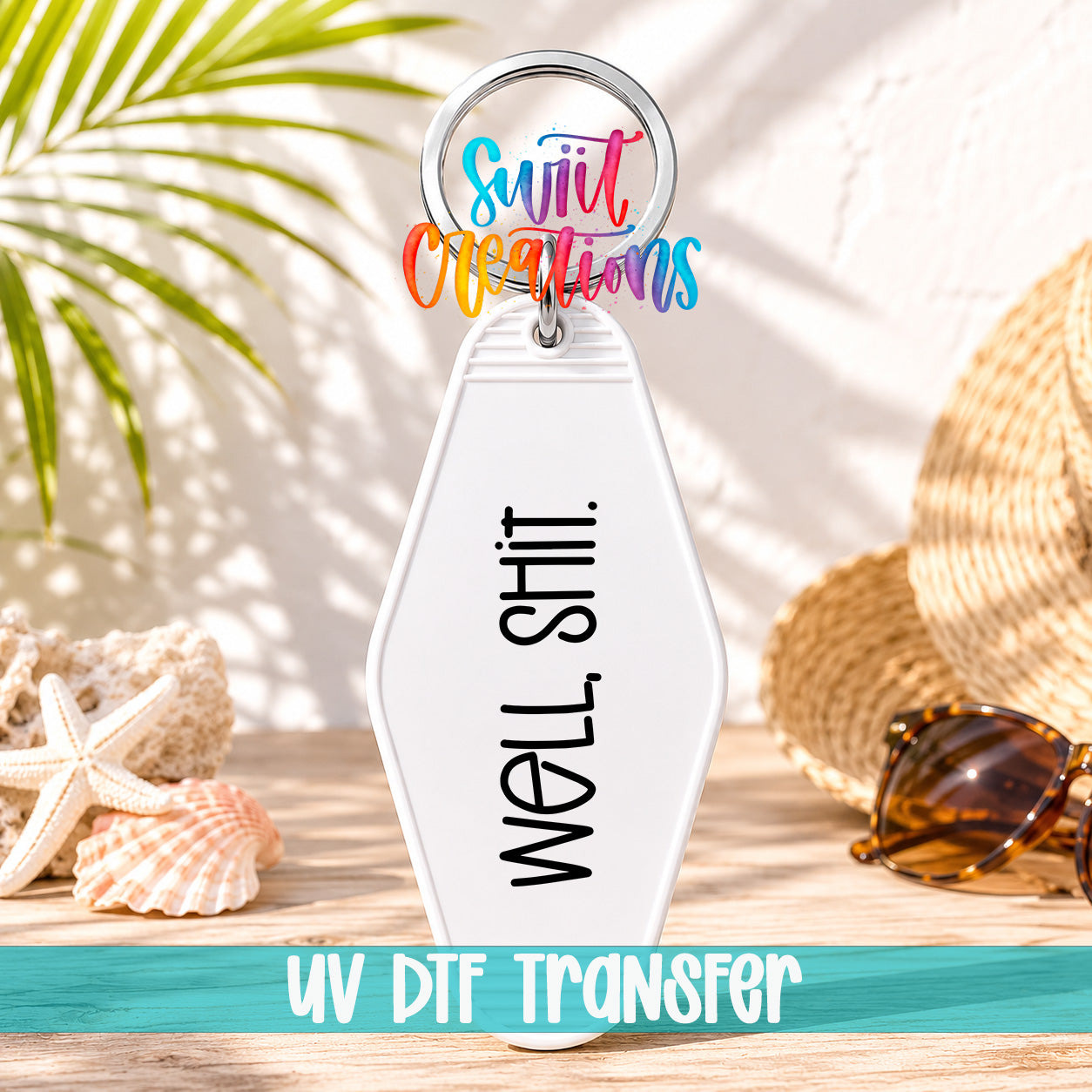 A keychain with the text "WELL SHIT" printed on it, along with a colorful ring and sunglasses on a wooden surface.