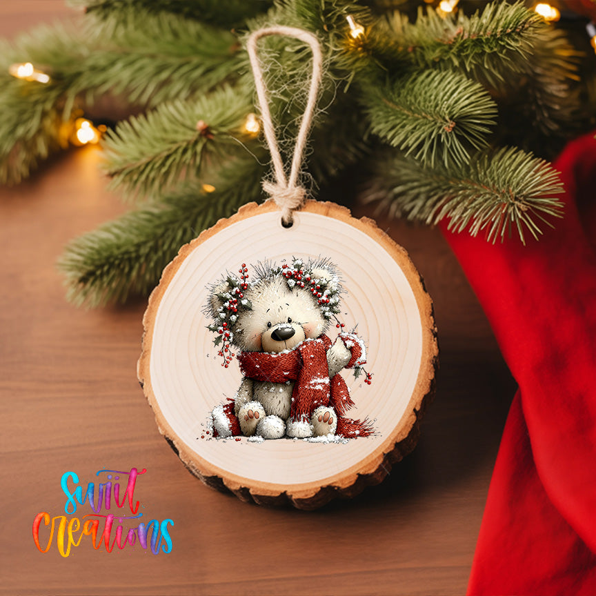 A wooden ornament featuring a teddy bear wearing a red scarf and a wreath, hanging on a Christmas tree.