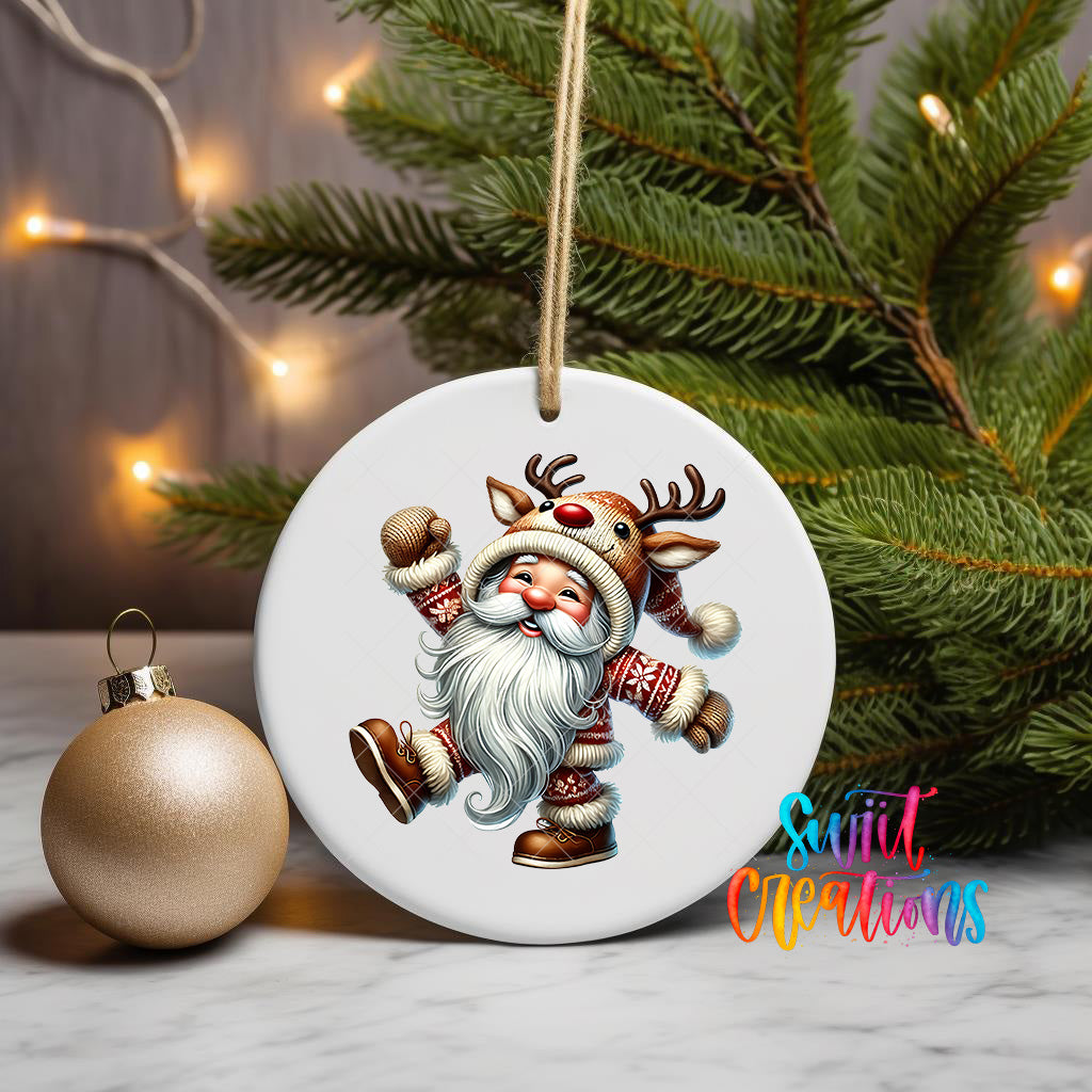 A white ceramic ornament featuring a smiling reindeer character is displayed on a white surface, with a Christmas tree and a gold ornament visible in the background.