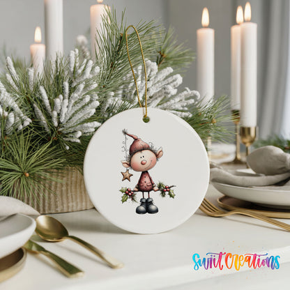A white ornament featuring a cartoon elf holding a star and holly is displayed on a table, surrounded by candles and greenery.