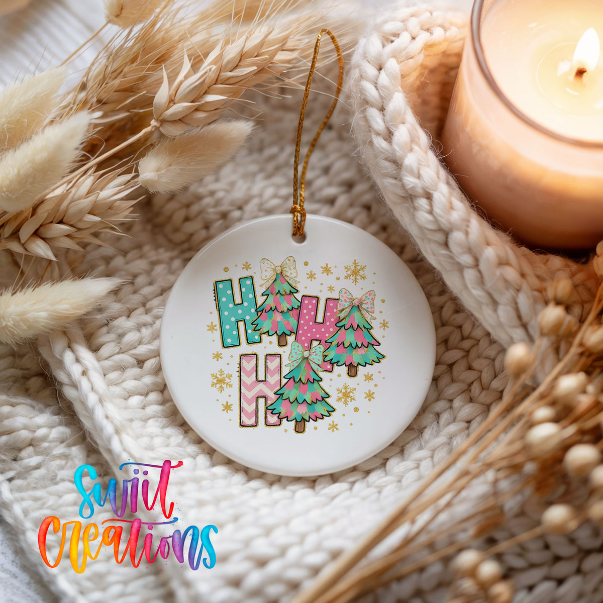 A white ceramic ornament with a colorful design hangs on a white knit blanket, surrounded by dried flowers and a lit candle.