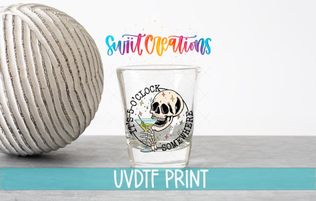 a shot glass with a skull design and the text "The 5 o'clock clock somewhere here" printed on it, along with a colorful background that includes the text "Swift Creations" and "UVDF PRINT".